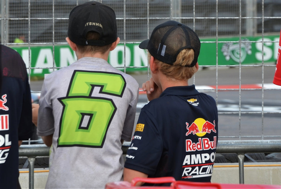 Two boys wearing caps and racing shirts watch event